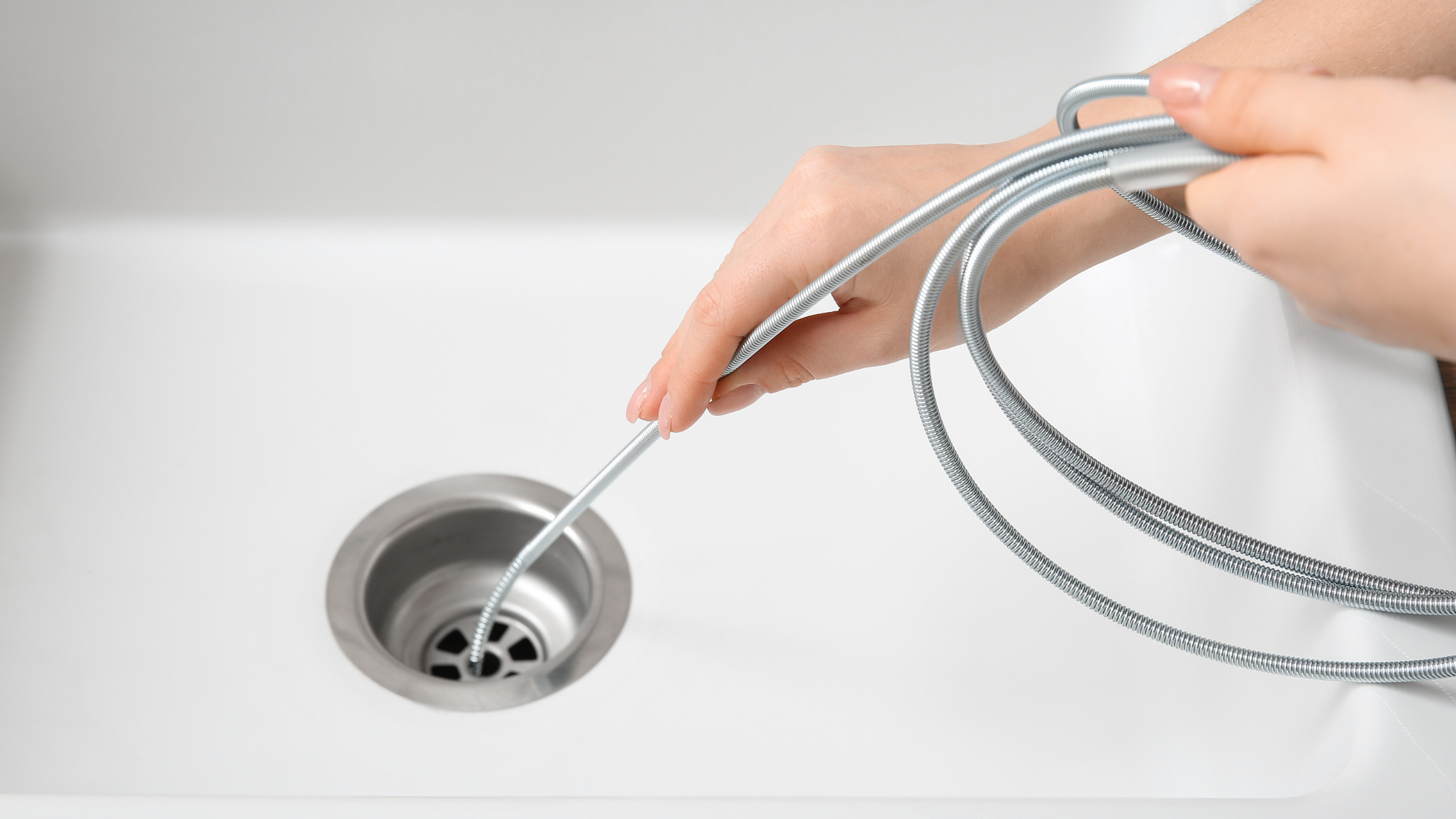 A Drain Bros llc technician clears a clogged kitchen drain with a plumbing snake before bigger repairs are considered.