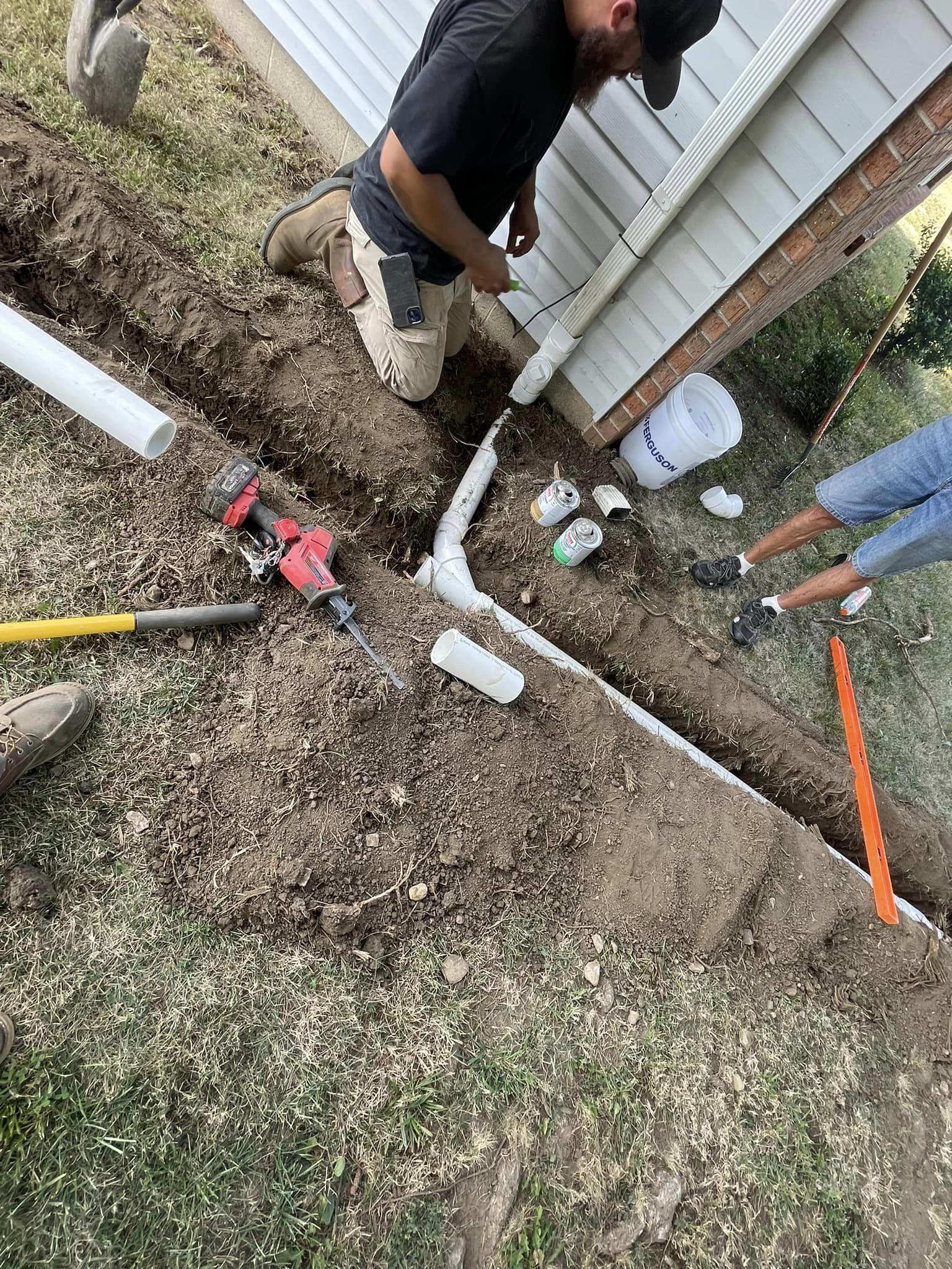 Drain Bros llc team installs a drainage system outside a house, working together to fix plumbing and improve water flow.