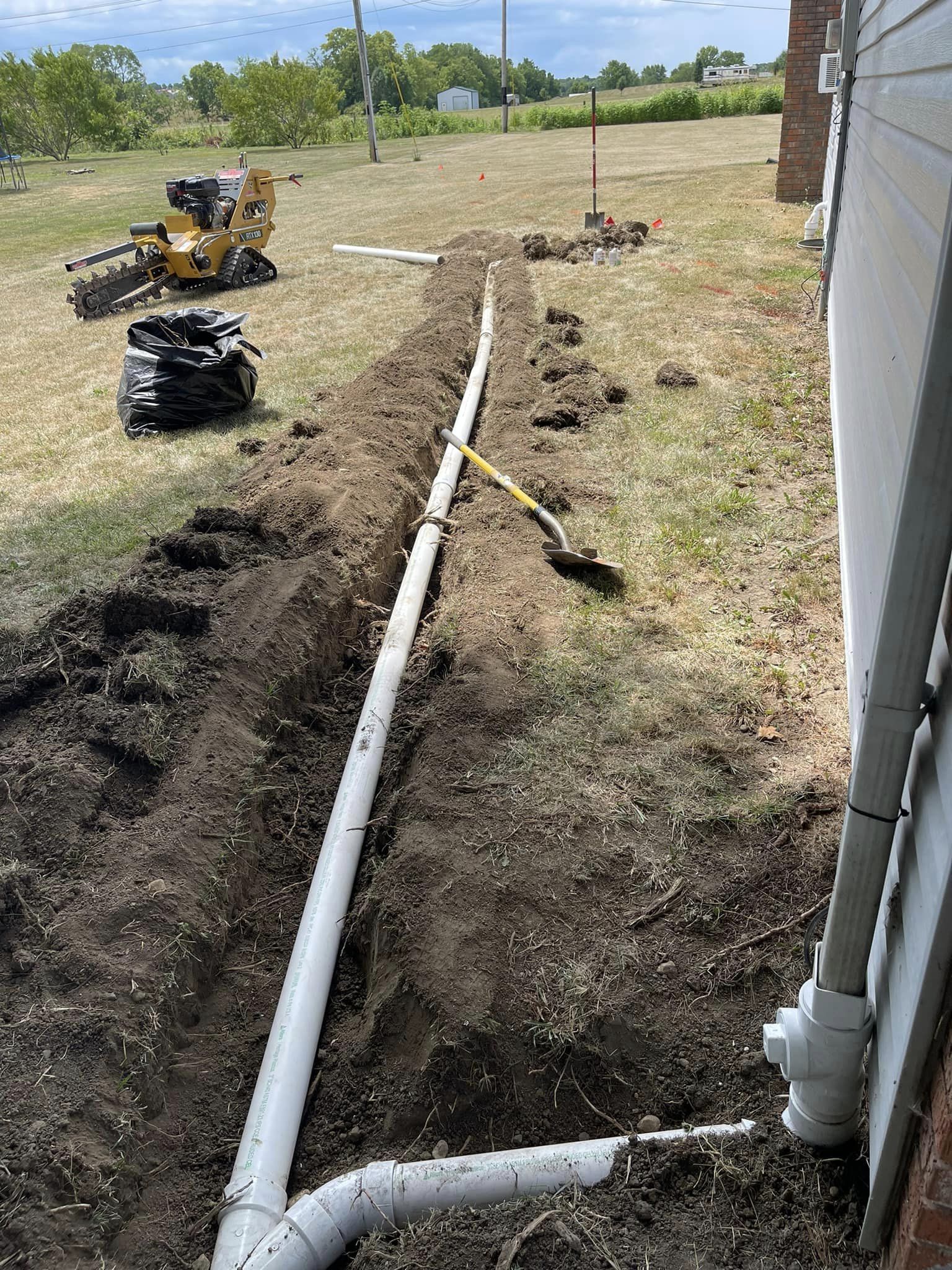 Drain Bros llc installs new drainage pipes for a house, showing their work in progress with equipment on site.