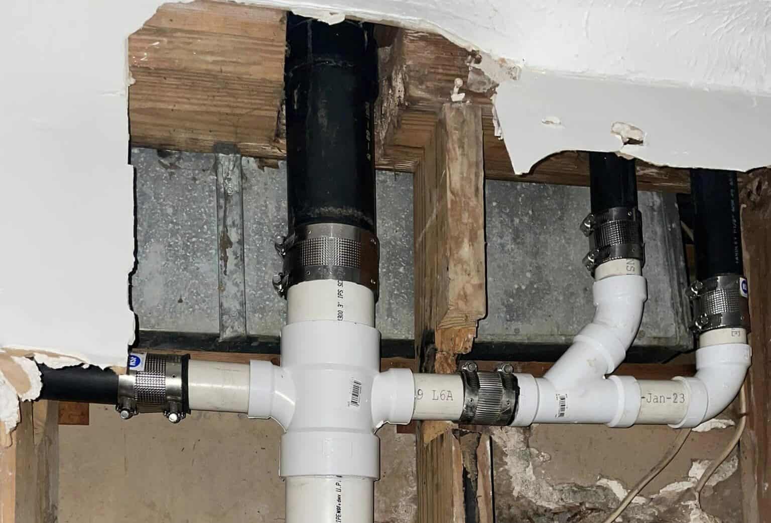 Drain Bros llc fixing sewer lines inside a wall; pipes and repairs are clearly visible due to damage.