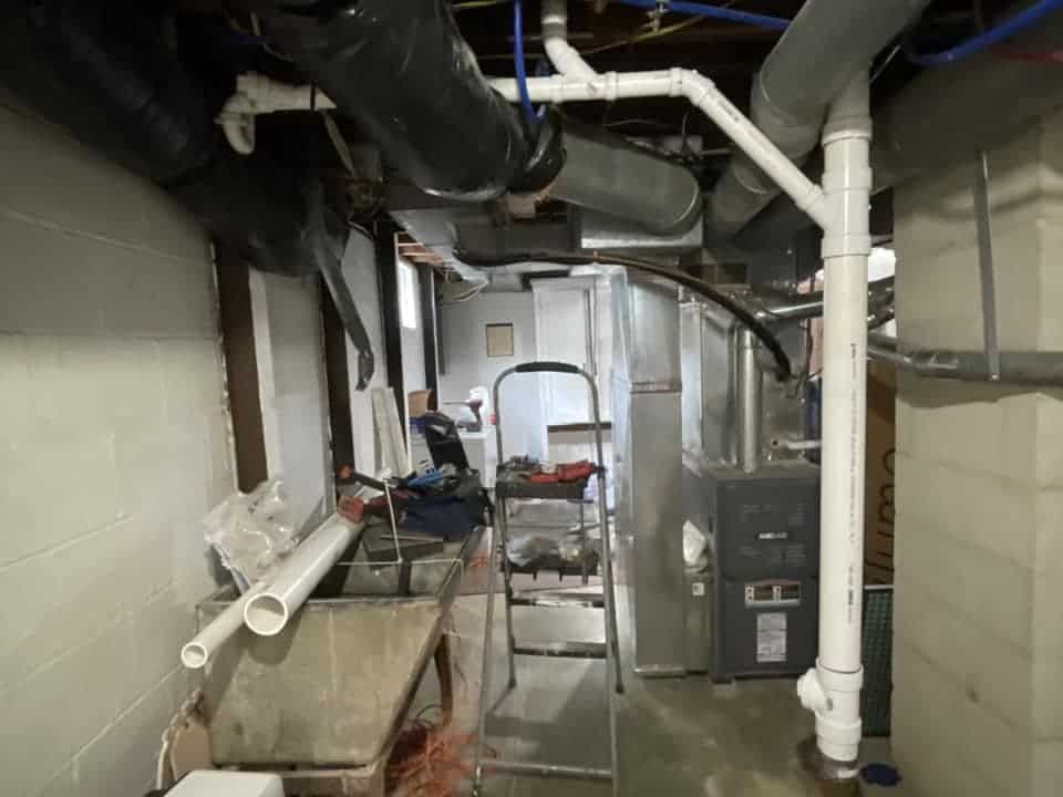 Drain Bros llc can help with sewer line issues shown by exposed pipes and tools in this unfinished basement.