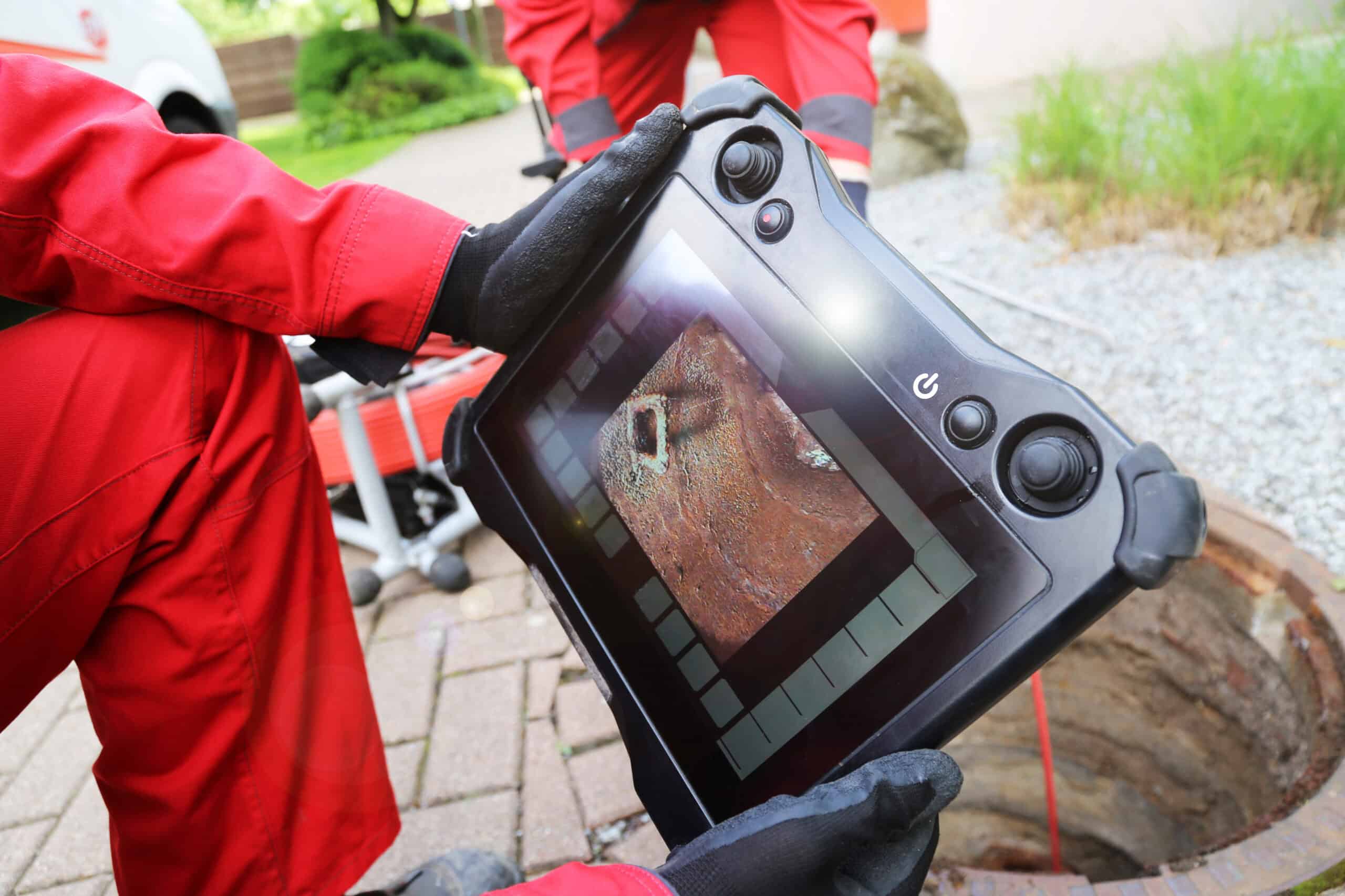 A Drain Bros llc worker reviews a plumbing camera inspection on a tablet at a job site, showing their service in action.