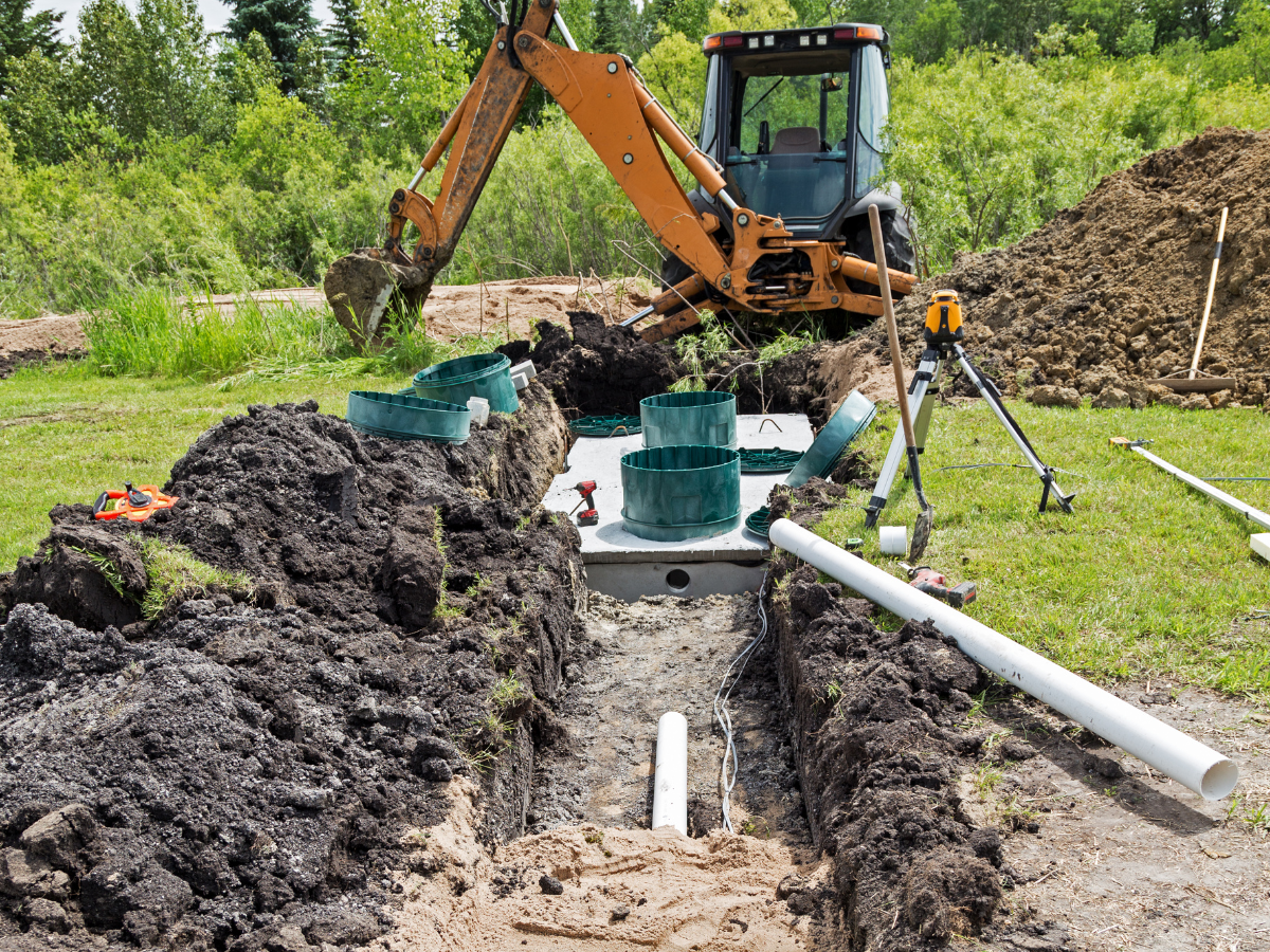 Drain Bros llc installs a drainage system using a backhoe, showing clear work progress on site.
