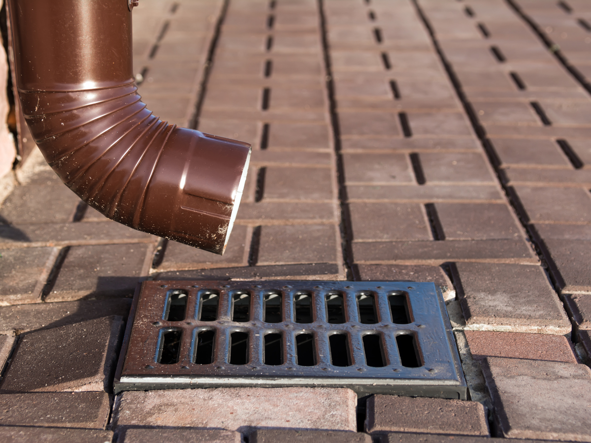 Drain Bros llc shows how their drainage system guides rainwater from a roof gutter safely into a sidewalk storm drain.