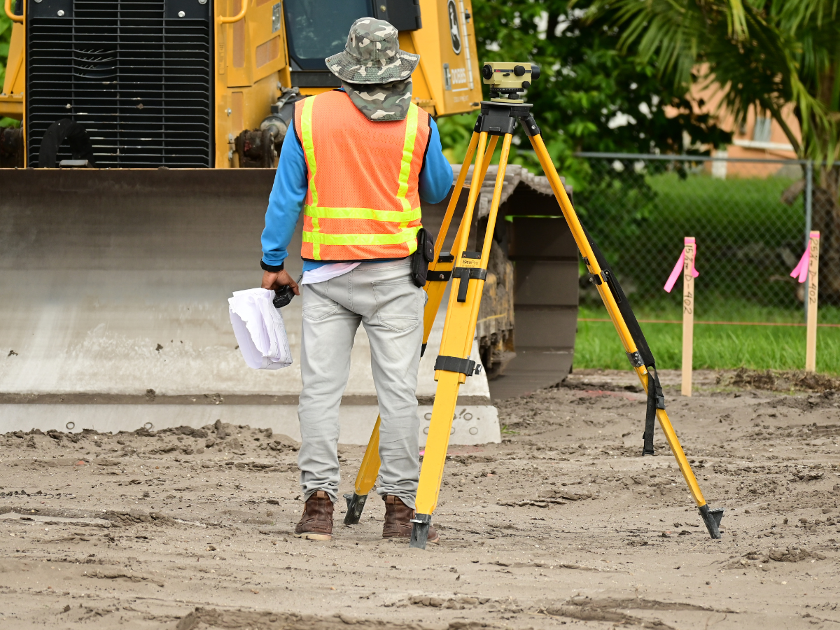 A Drain Bros llc worker checks plans and equipment while managing septic system installation at a marked jobsite.